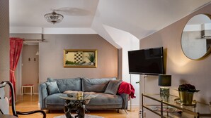 A living room with a grey sofa, a glass coffee table, a TV, a chandelier, and a red curtain. - Hotel Vännäs (Vannas)
