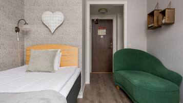 A room with a bed, a green sofa, a wall-mounted light fixture, and a door with a sign.