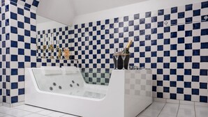 A modern bathroom with a checkered tile wall, a freestanding bathtub, and a champagne bottle on the counter. - Hotel Vännäs (Vannas)