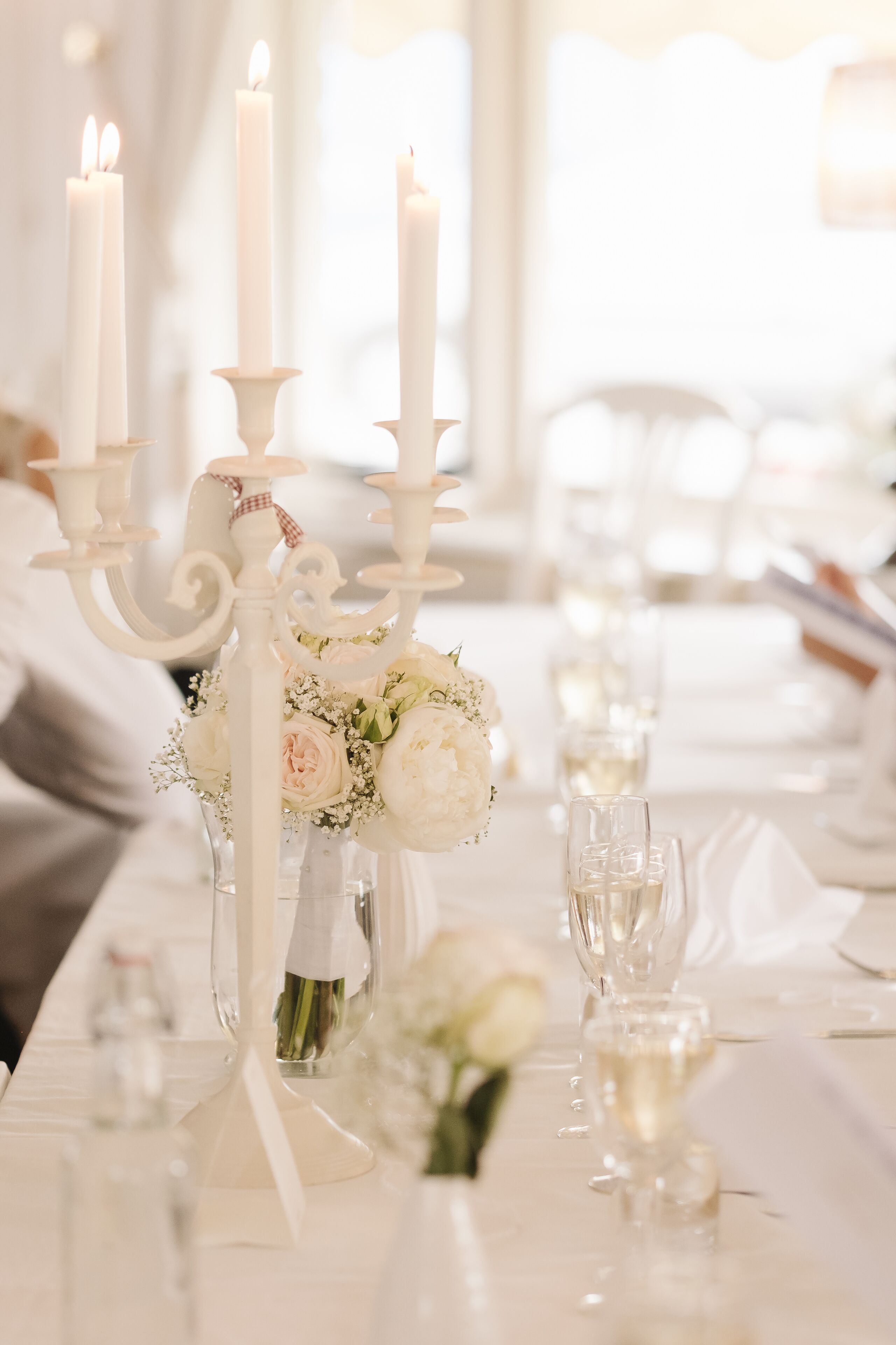 A table set with white candles, a vase with flowers, and wine glasses.