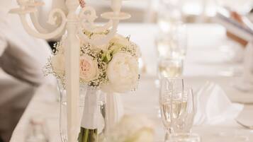 A table set with white candles, a vase with flowers, and wine glasses.