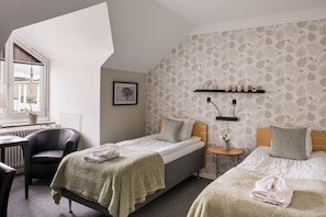 A room with two beds, a desk, a chair, and a radiator.