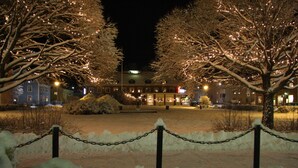 A hotel with a snow-covered courtyard, chain-link fence, and illuminated trees. - Hotel Vännäs (Vannas)
