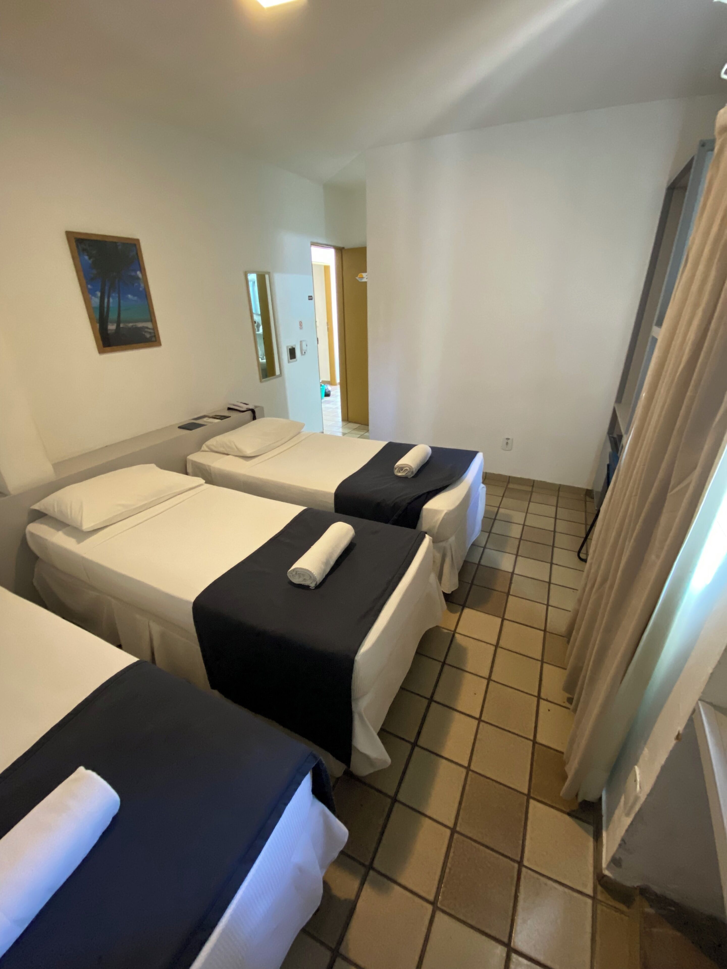 A hotel room with two beds, a painting on the wall, and a tiled floor.
