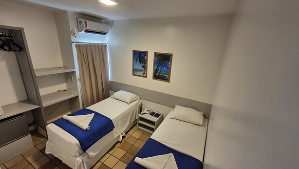 A hotel room with two beds, a desk, a wardrobe, an air conditioning unit, and two framed pictures on the wall. - Bluemar Hotel (Maceió)