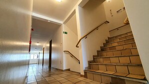 A hotel corridor with a tiled floor, a staircase with handrails, and a door with an emergency exit sign. - Bluemar Hotel (Maceió)