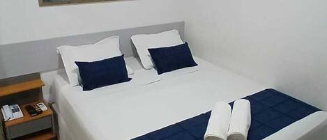 A hotel room with a bed, a nightstand, a painting, and a tiled floor.