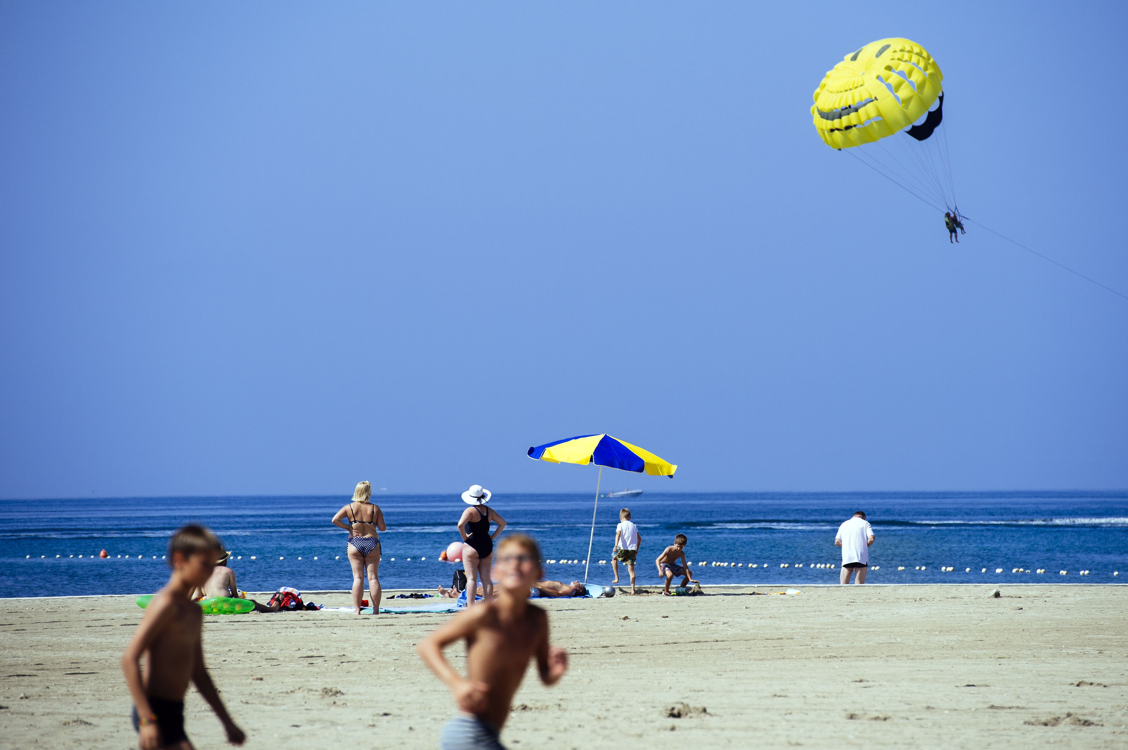 A beach scene with people, a parasail, and a blue and yellow umbrella.