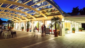 Un espacio al aire libre con techo de vidrio, plantas en macetas y disposición de asientos.