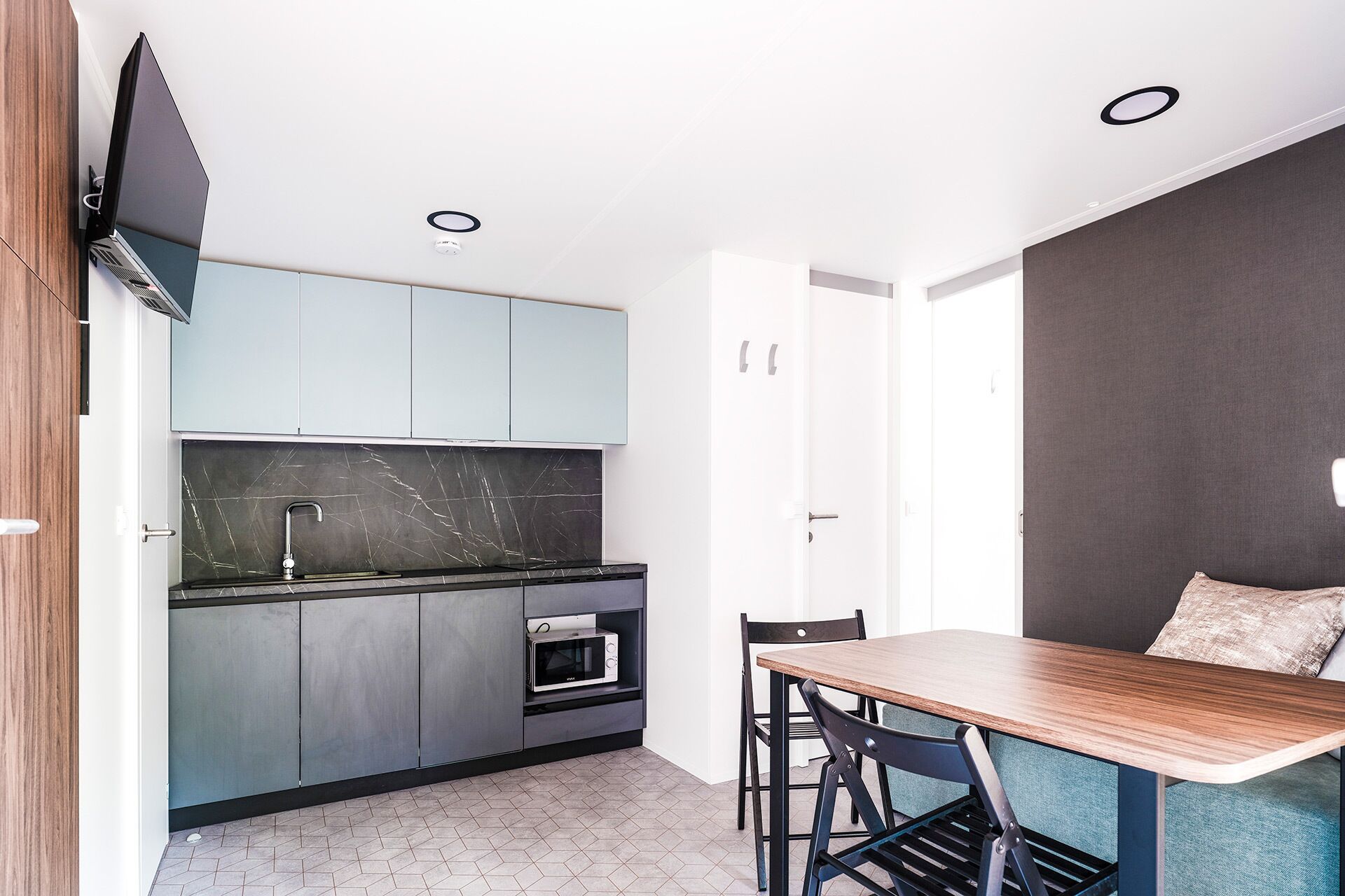 Een moderne keuken met een inbouwoven, een magnetron en een spoelbak. Er is een eethoek met een tafel en stoelen.