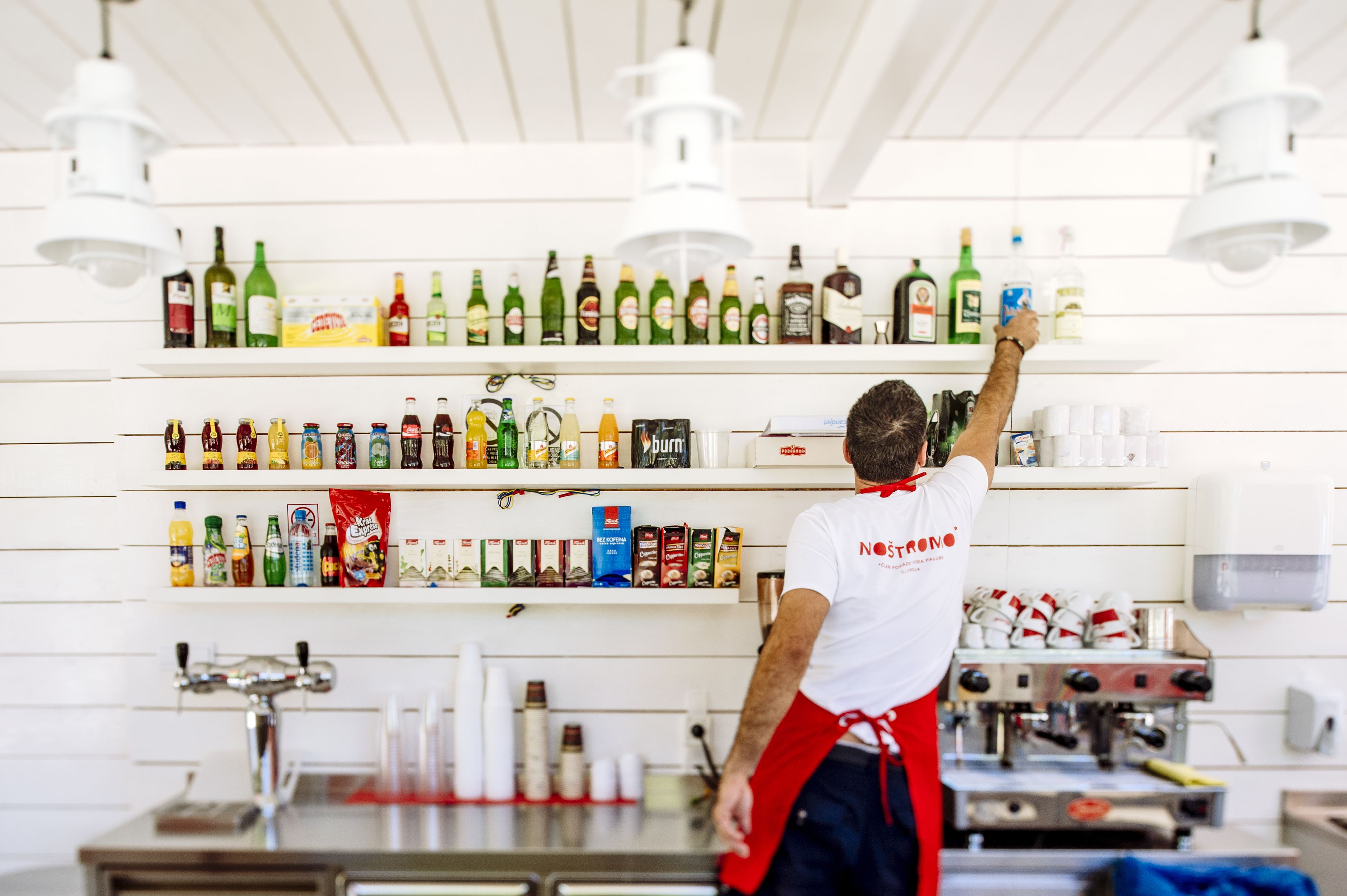 Une personne est en train de ranger des boissons et des en-cas variés sur les étagères d’une cuisine bien aménagée.