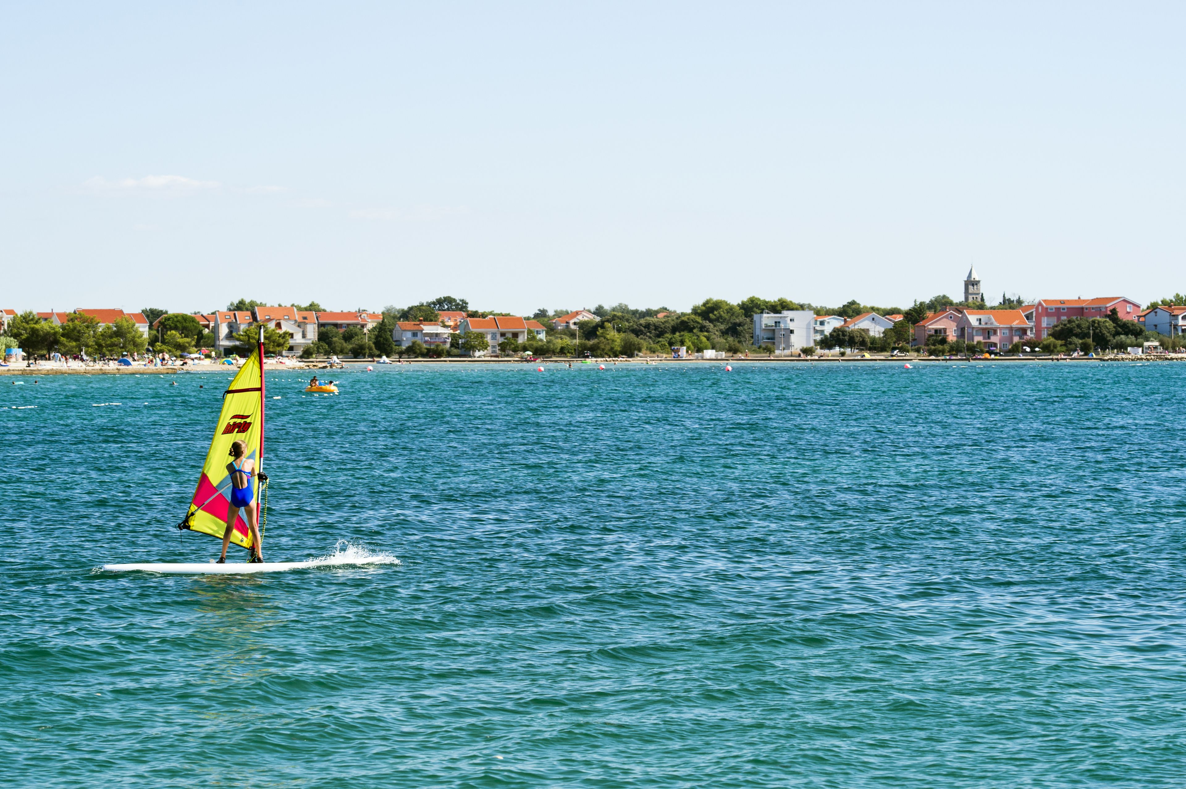 A person windsurfing on a body of water with buildings in the background.
