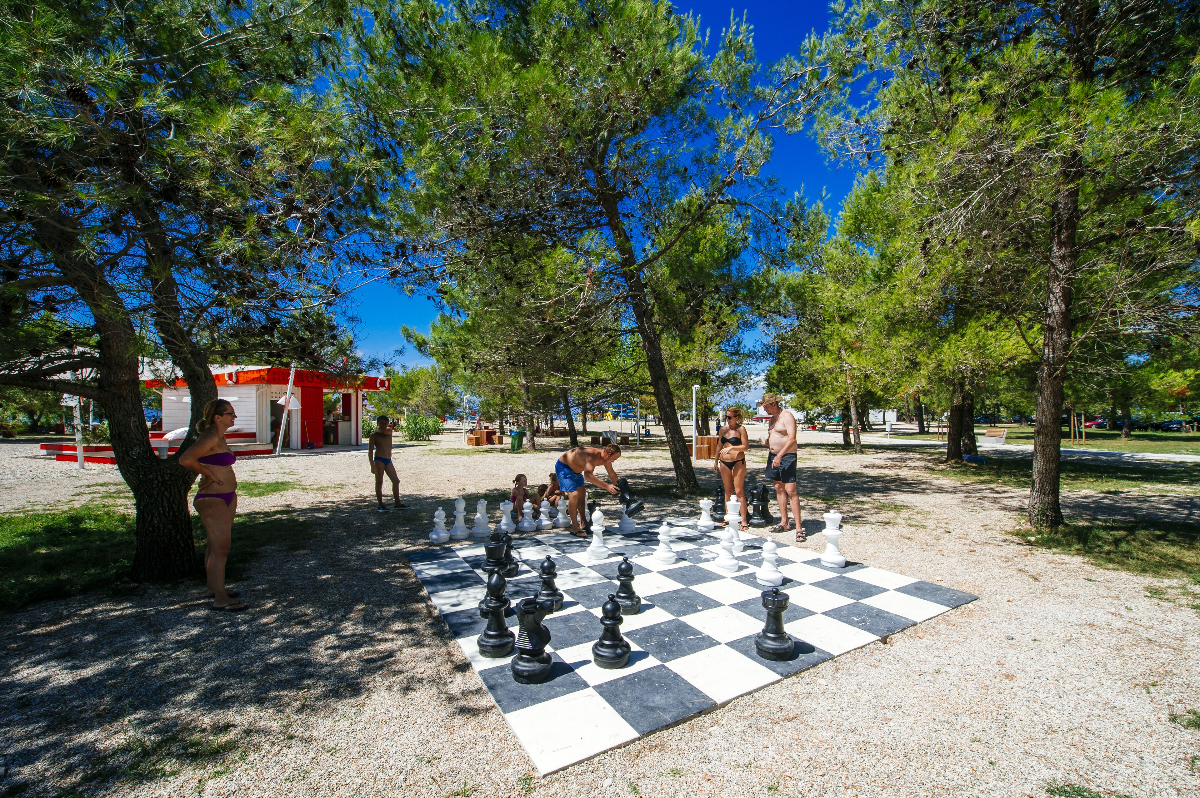 A chessboard set up outdoors with people playing.