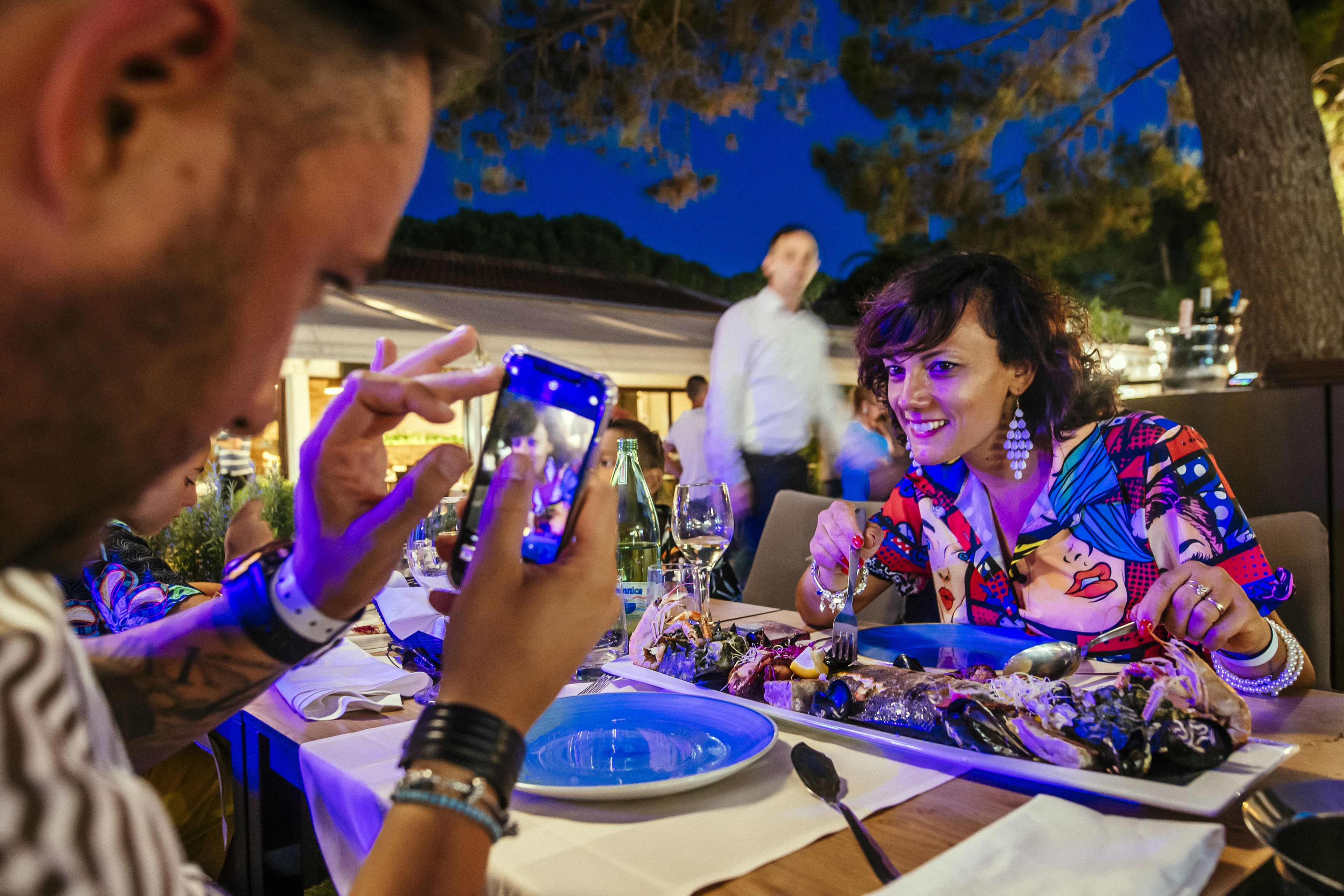 Una mesa de comedor con platos de comida, una copa de vino y un teléfono inteligente.