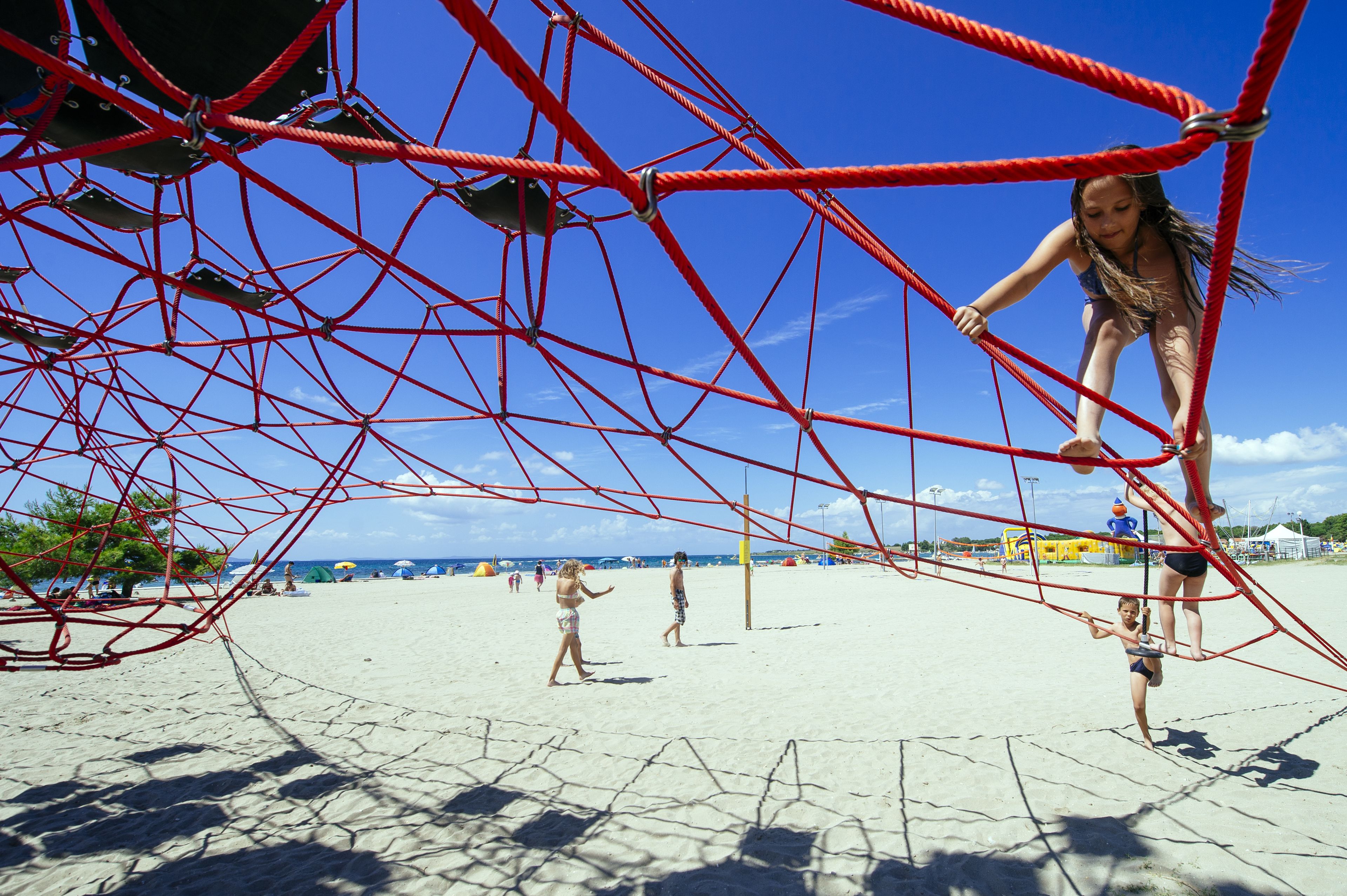 Una playa con una estructura roja para escalar tipo cuerda.
