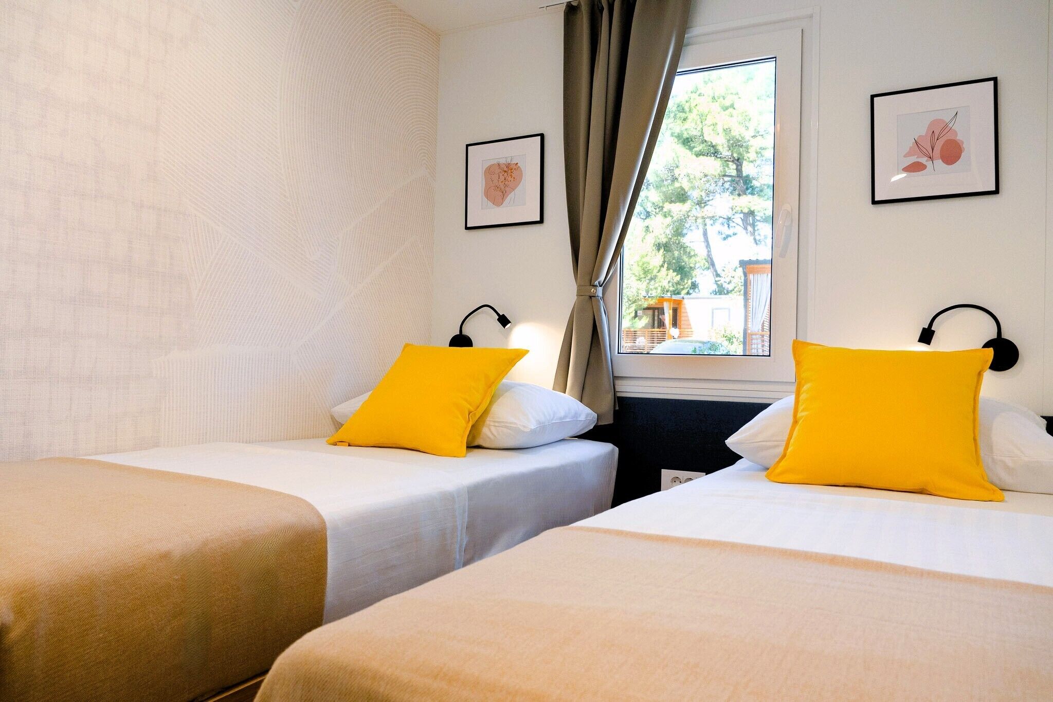 A hotel room with two single beds, each with a yellow pillow and a black lamp on the nightstand.