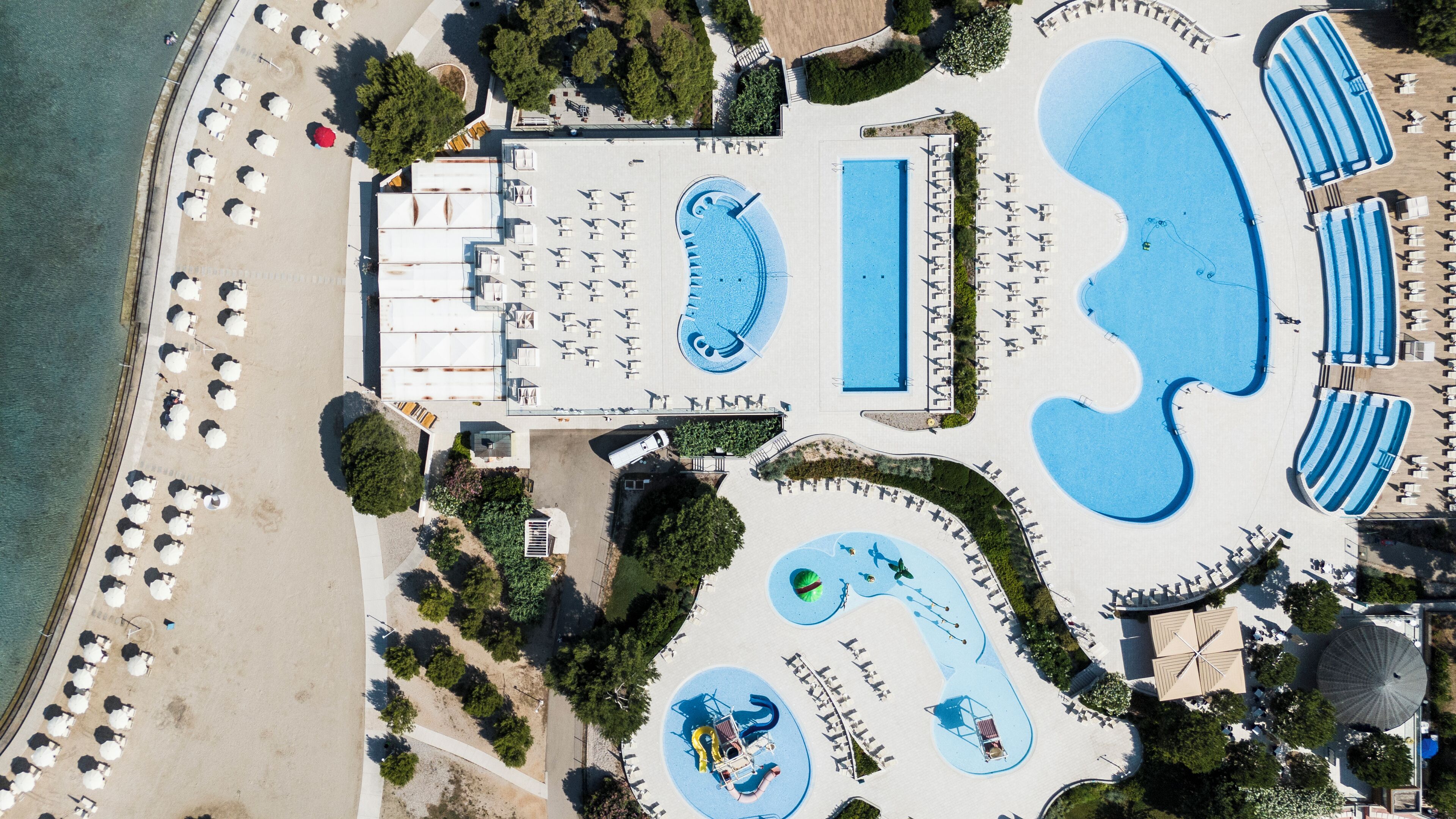 Vue aérienne d’un complexe hôtelier doté de plusieurs piscines, de chaises longues et d’une plage.