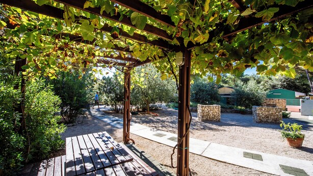 A covered outdoor area with a wooden bench, stone walls, and a pergola with vines. - Zaton Holiday Resort Camping homes (Nin)