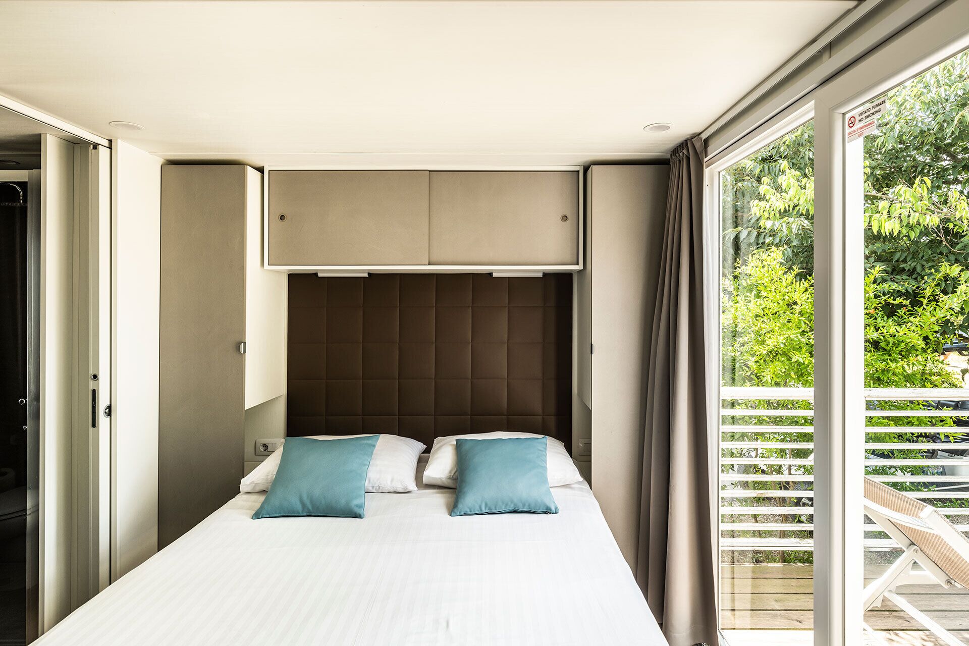A bedroom with a bed, two pillows, a headboard, and a window with curtains.