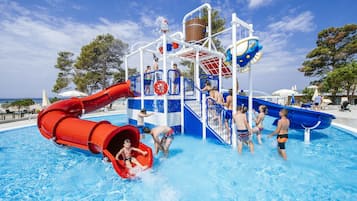 Ein Wasserpark mit roter Wasserrutsche, blauem Wasserspielbereich und Schwimmbecken.