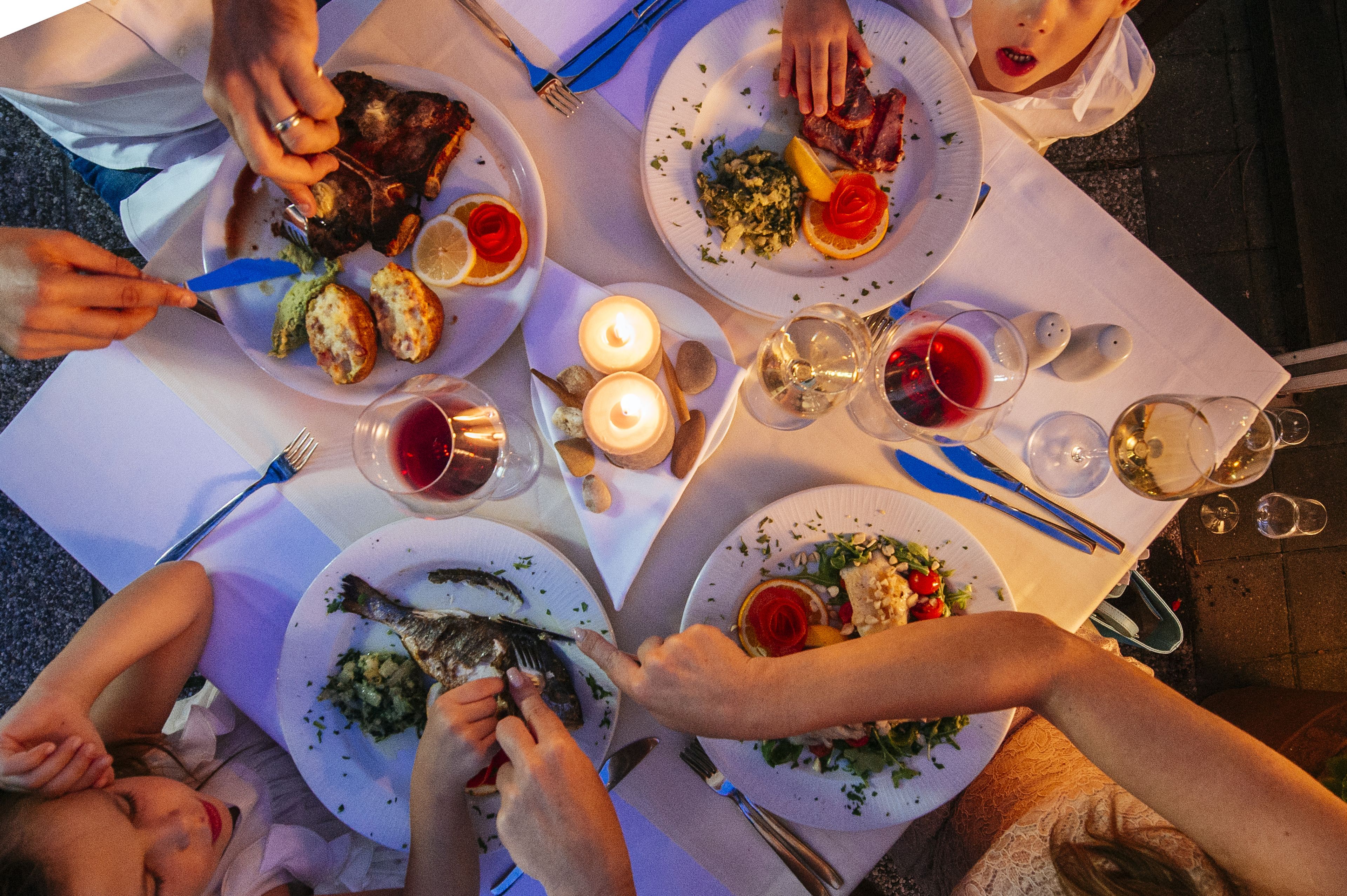 Een groep mensen dineert aan een buitentafel met borden eten, wijnkannen en kaarsen.