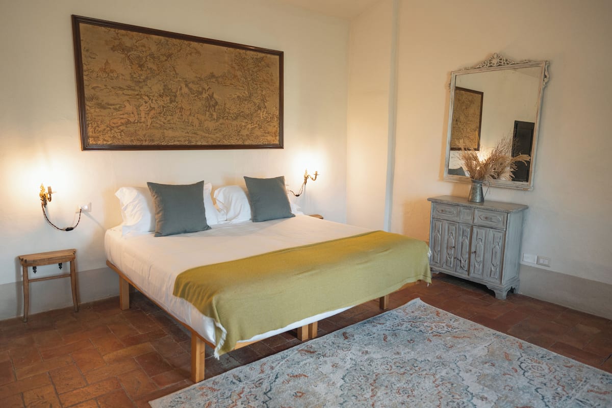 Ein Schlafzimmer mit Bett, Nachttischlampen, einem Nachttisch, einer Kommode und einem großen gerahmten Bild an der Wand.