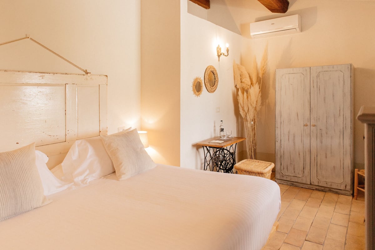 Ein Schlafzimmer mit einem Bett, einem kleinen Tisch mit Lampe, einem Zier-Spiegel und einem Kleiderschrank.
