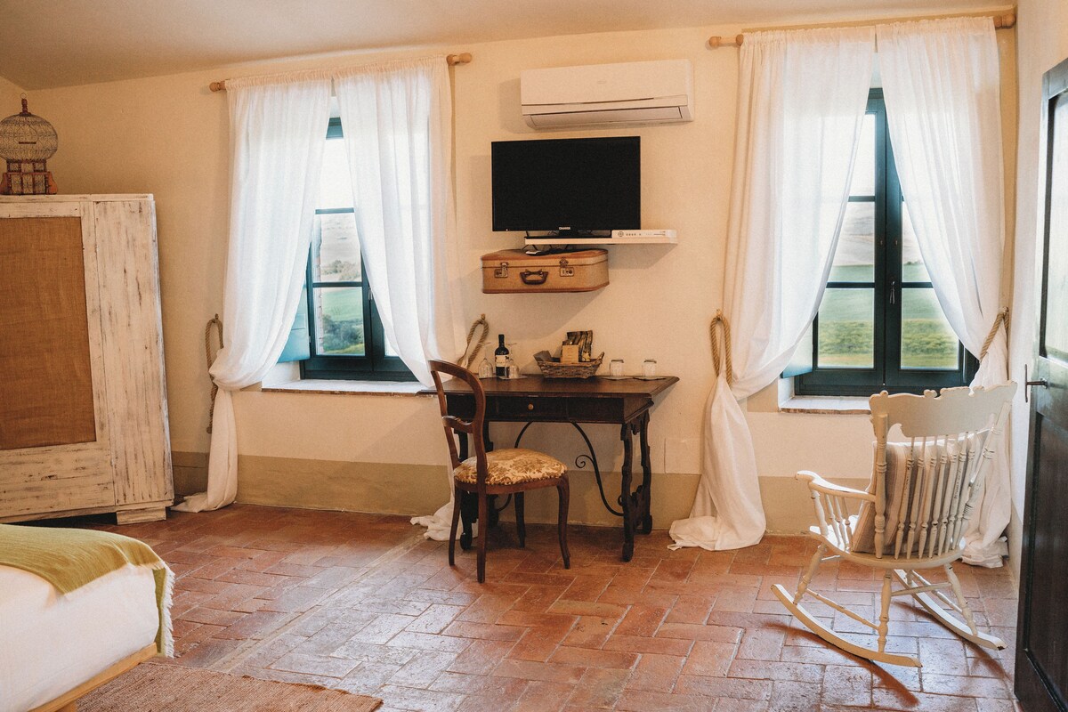 Una habitación con un escritorio de madera, una silla, un televisor montado en la pared y un sillón mecedora.