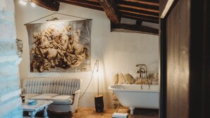 Une salle de bain avec une baignoire, un grand tableau accroché au mur, un banc rembourré et un plancher en bois rustique.
