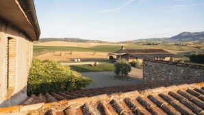 Un bâtiment rustique, doté d’un toit en tuiles, qui surplombe un paysage rural composé de champs et, au loin, d’une montagne.