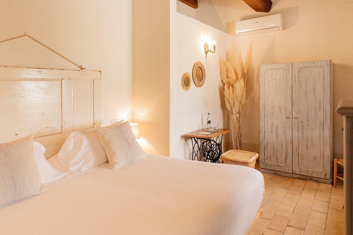 A bedroom with a bed, a small table with a lamp, a wardrobe, and decorative wall sconces.