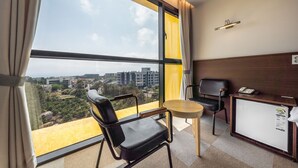 A hotel room with a large window, a desk, a chair, and a small table. - Sunrise Hotel Jungmun (Seogwipo)