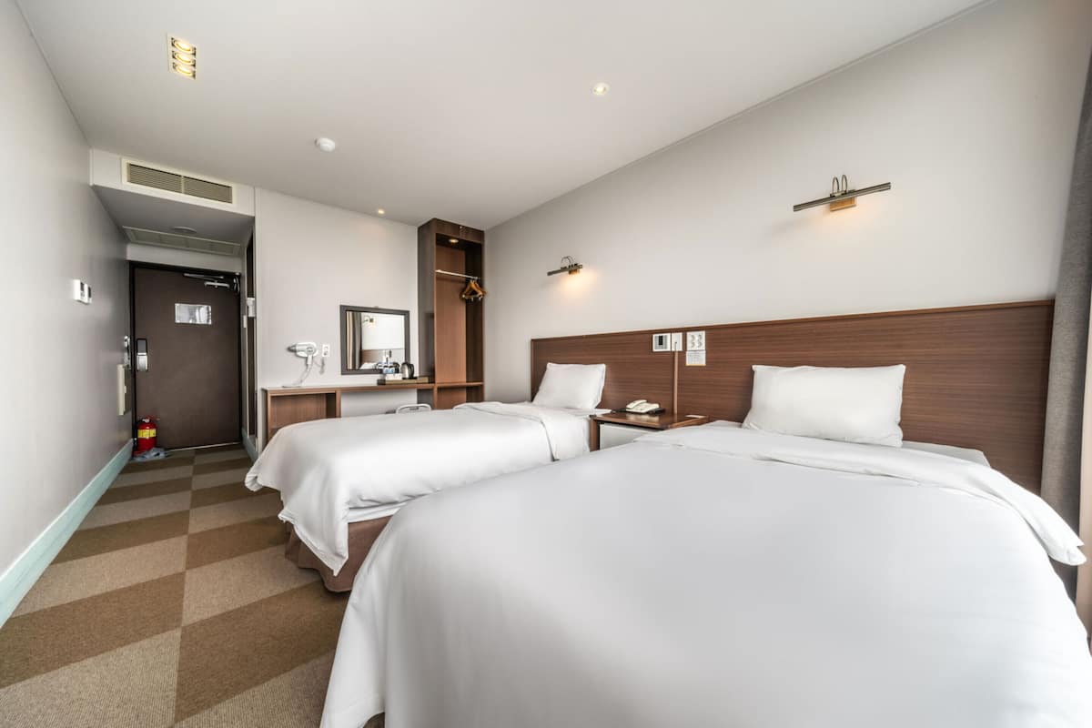 A hotel room with two beds, a desk, a mirror, and a wardrobe.