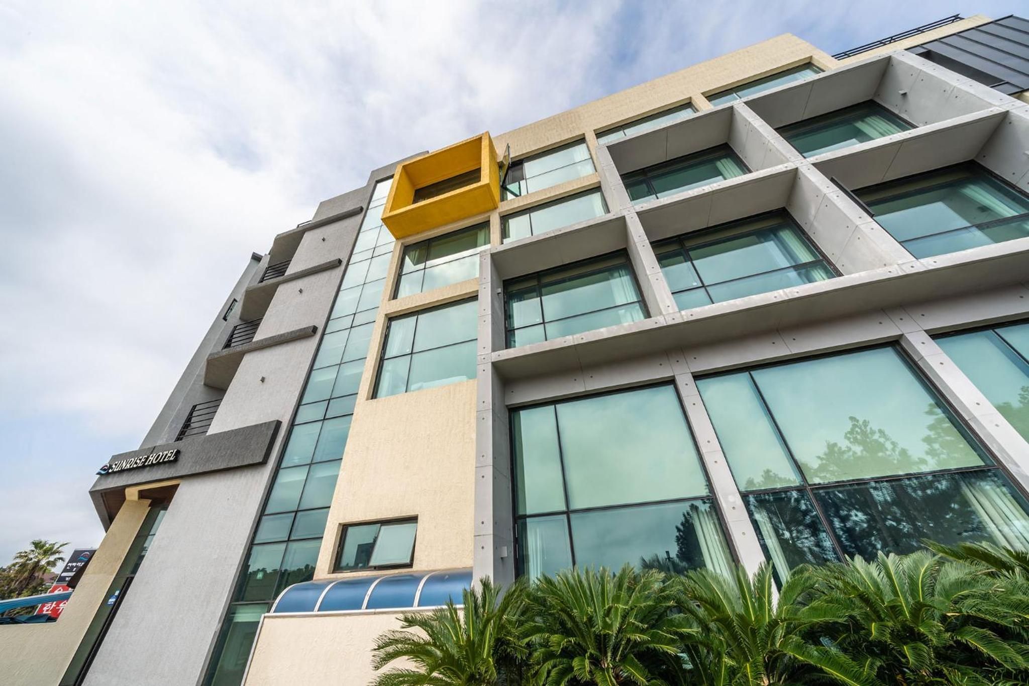 A modern hotel building with multiple floors, large windows, and a distinctive yellow structure on the upper level.