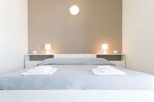 Un letto rifatto con due cuscini, due comodini con lampade e un punto luce a parete.