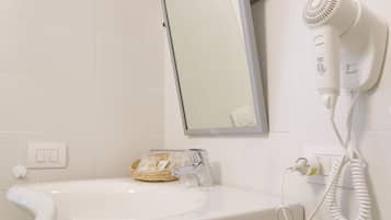 Uma casa de banho com uma pia branca, um espelho, um secador de cabelo e um cesto de produtos de higiene pessoal.