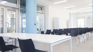 A conference room with a long white table, rows of black chairs, and large windows with blinds. - Hotel Campus Sanpaolo (Turin)
