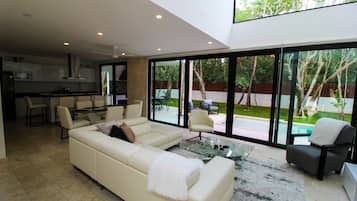 A modern living room with a sofa, armchairs, and a coffee table. There is a kitchen in the background with a dining area.