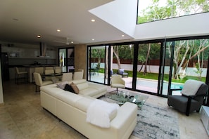 A modern living room with a sofa, armchairs, and a coffee table. There is a kitchen in the background with a dining area. - Bahia Principe Vacation Rentals - Four-Bedroom House (Akumal)