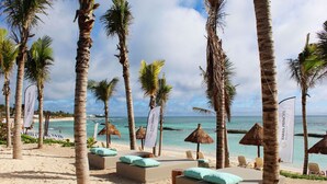 Un resort en la playa con sombrillas de techo de paja, sillas de descanso y palmeras.