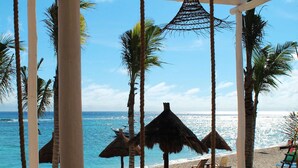 Un salón junto a la playa con una mesa de madera, sillas de descanso y sombrillas de paja.