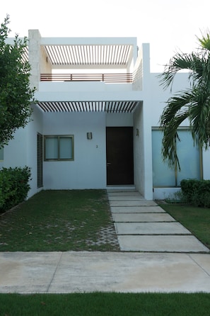 Una casa moderna de dos pisos con techo plano, un patio cubierto y una puerta principal.