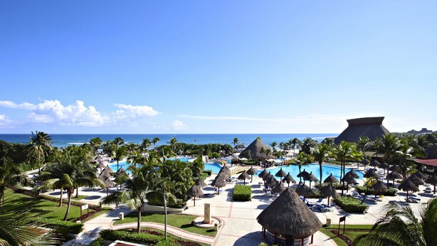 A resort with multiple swimming pools, palm trees, and a view of the ocean.