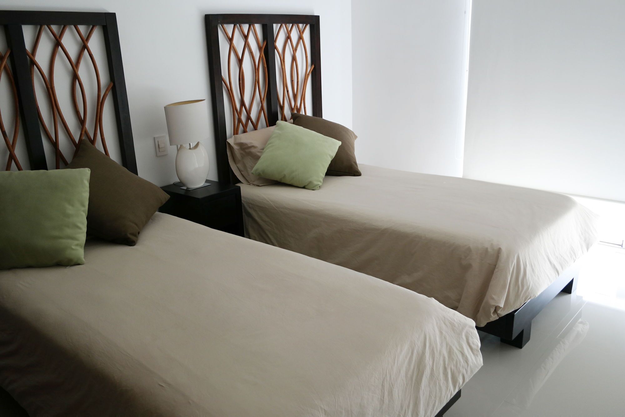 Due letti singoli con biancheria beige, un comodino con una lampada e una testiera decorativa.