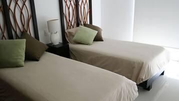 Due letti singoli con biancheria beige, un comodino con una lampada e una testiera decorativa.