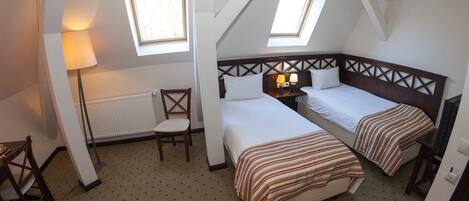 A room with two beds, a chair, a table, and a radiator.