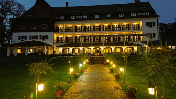 A large, multi-story hotel with a central entrance, a stone pathway leading to the entrance, and outdoor lighting. - Hotel Gradina Morii (Sighetu Marmatiei)