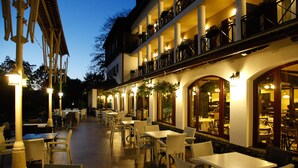 An outdoor dining area with wicker chairs and tables, a covered walkway, and a building with multiple balconies. - Hotel Gradina Morii (Sighetu Marmatiei)