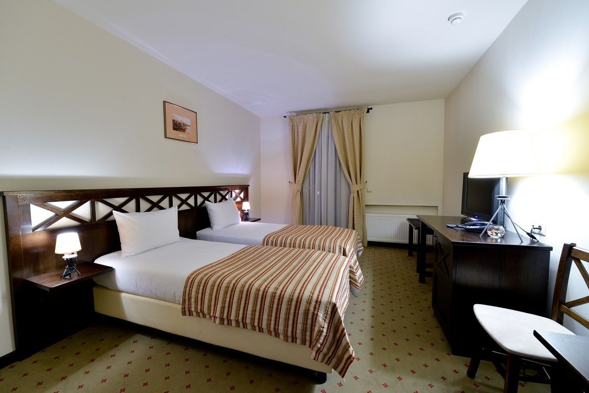 Ein Hotelzimmer mit zwei Betten, einem Schreibtisch, einem Sessel und einem Fernseher.