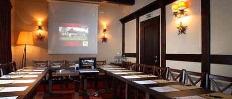 A conference room with a long table, chairs, a projector screen, and wall-mounted lamps.